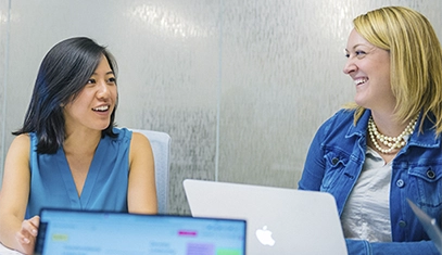 two women working on their laptops and smiling