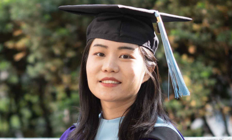 Xiangyi Liu Looks at the camera while wearing her graduation gown and regalia