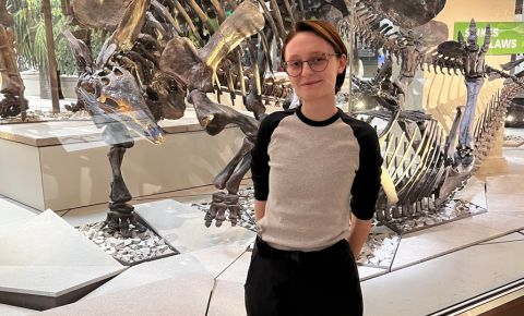 An image of Sylvia standing in front of a dinosaur exhibit.