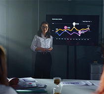 A woman presents a multicolored chart to a small audience
