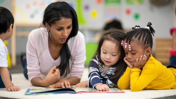A teacher and elementary students read a picture book together.