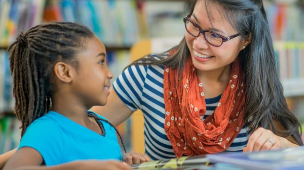 A teacher helps an elementary student read a book.