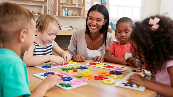 A teacher supports elementary students working with learning materials at a classroom table.