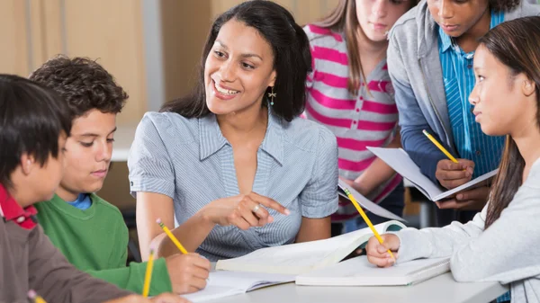 A teacher guides a group of secondary students through classroom work.