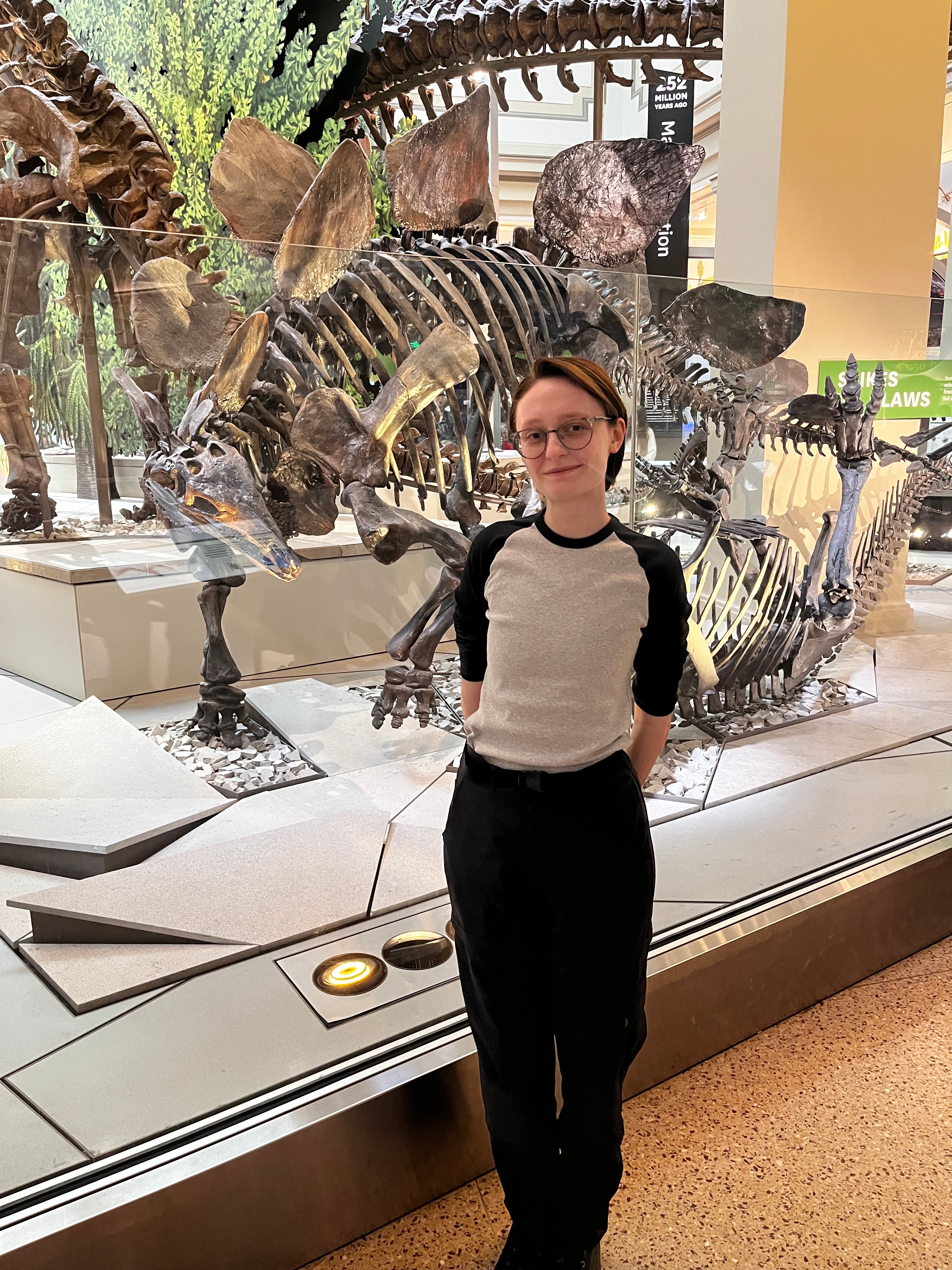 An image of Sylvia standing in front of a dinosaur exhibit.