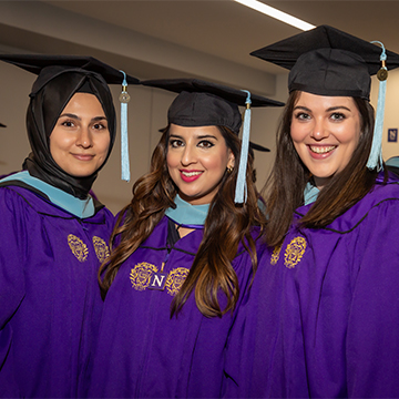 Three students in graduation attire smile towards the camera. Their regalia is purple.