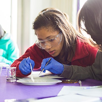 Teenage girl wearing goggles and gloves working with a plate of liquid